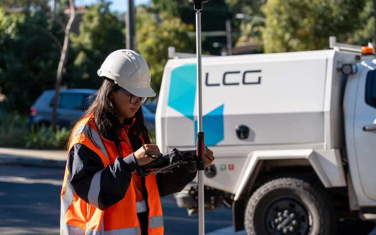 LCG surveyor with a GPS rover beside a branded LCG field vehicle